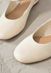 Cream leather flats with a rounded toe and an open cutout at the sides, featuring a smooth texture and minimalistic design.