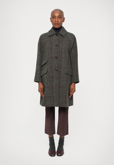 Manteau à chevrons gris avec un col, trois boutons et des poches latérales, associé à un pantalon court violet, des chaussettes grises et des chaussures bordeaux.