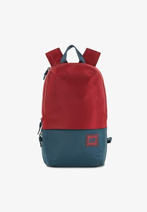 Mochila de poliéster roja y azul con correas de hombro acolchadas, compartimentos dobles con cremallera y un parche de logo en el frente. Textura suave, forma rectangular.