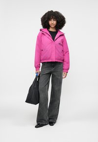 Bright pink puffer jacket with a hood, elastic cuffs, and a front zipper. Paired with high-waisted wide-leg gray jeans and a black tote bag.