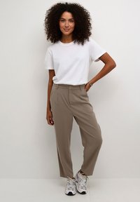 Bézs színű, magas derekú nadrág szabott kialakítással és oldalzsebekkel, egyszerű fehér pólóval és szürke sportcipővel párosítva.