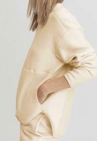 Kremowy, oversize'owy sweatshirt z teksturowanej tkaniny, z opadającymi ramionami, bocznymi kieszeniami i widocznymi detalami szwów.
