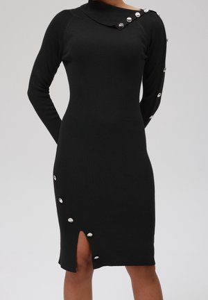 Robe pull noire ajustée à manches longues avec détails de boutons argentés sur l'épaule, la manche et une fente diagonale près du genou.