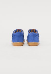 Scarpe in suede blu con una texture morbida, dotate di una suola in gomma beige e una striscia in Velcro per una chiusura facile. Design semplice senza ulteriori dettagli.
