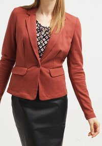 Blazer couleur rouille en tissu lisse avec une coupe ajustée. Comprend des revers crantés, deux poches avant et une fermeture à un bouton.