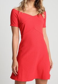 Vestido rojo de canalé con mangas cortas, diseño con escote off-the-shoulder y falda acampanada. Presenta detalles de costura diagonal en el corsé.