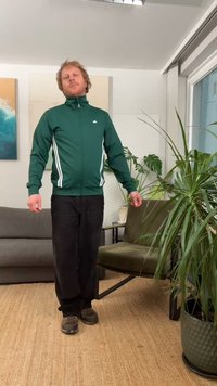Green zip-up jacket with white stripes along the sides, paired with dark pants and brown shoes. Indoor setting with plants and furniture.