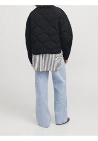 Černá prošívaná bunda s poplinovými pruhy uvnitř, se zaobleným výstřihem a uvolněným střihem, v kombinaci s světle modrými širokými džíny.