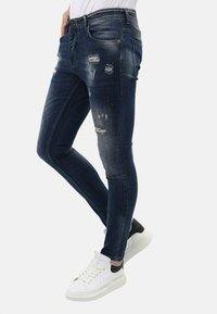 Skinny-fit blauwe denimjeans met verwoeste details en vervaagde patches. Gepaard met witte sneakers met zwarte accenten.