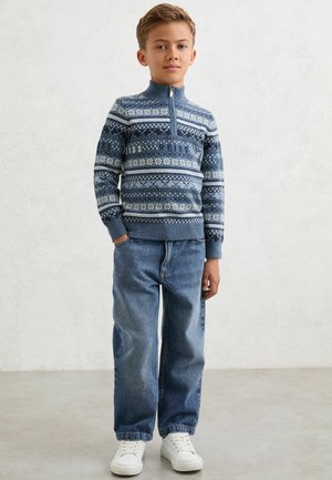 Mėlynas megztas džemperis su baltais raštiniais akcentais, užtrauktuku užsegamas apykaklė; derinamas su laisvomis mėlynomis džinsomis ir baltomis sportbačiais.