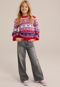 Rdeča in vijolična pulover s patterned vzorcem pingvinov, v kombinaciji s sivimi širokimi hlačami in rožnatimi supergami. Lase oblikovane v proste valove.