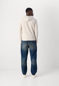 Lys beige hettegenser med slim fit og kenguru-lomme; kombinert med løstsittende, falmede blå denimjeans og hvite sneakers.