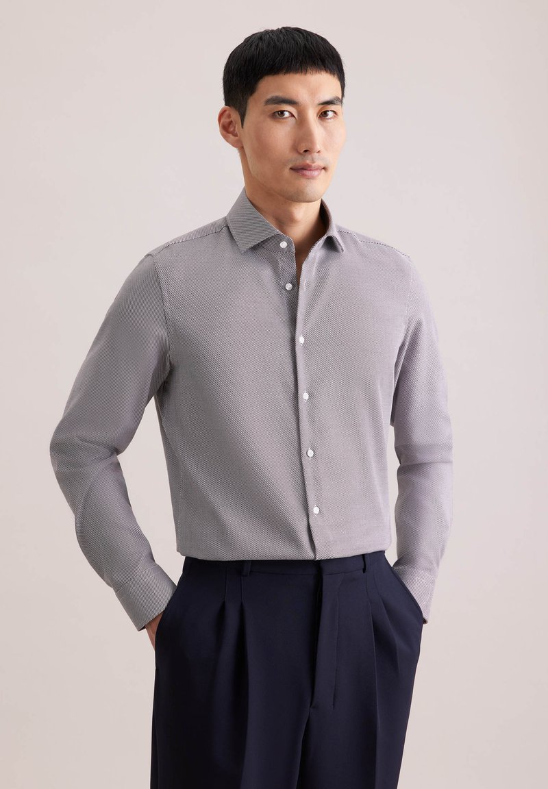 Camicia con bottoni in tessuto grigio chiaro testurizzato con un motivo sottile, colletto classico e maniche lunghe, abbinata a pantaloni scuri.