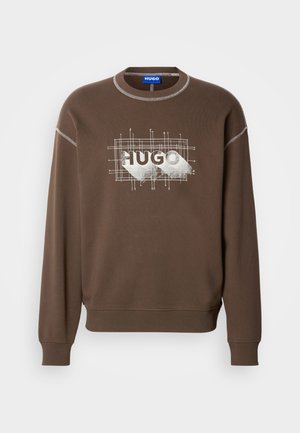 Hnedá mikina s dlhými rukávmi, na ktorej je biely grafický logo "HUGO". Okrúhly výstrih a rebrované manžety dodávajú textúru.