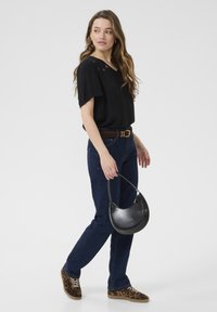 Haut noir à manches courtes avec un col en V, jeans bleu foncé, une ceinture en cuir marron, des chaussures à imprimé léopard et un sac à main noir courbé.