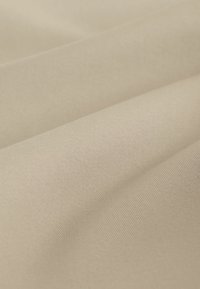 Tela beige suave con textura visible de tejido fino y pliegues suaves que crean sombras y reflejos delicados.