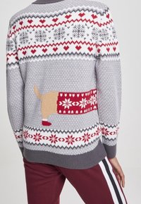 Grauer Strickpullover mit festlichem Design, das rote und weiße Schneeflocken, Herzen und ein detailliertes Hundemotiv auf der Rückseite zeigt.
