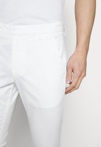 Witte katoenen broek met rechte snit, voorzien van zijzakken en een gladde textuur. De tailleband heeft lussen voor een riem en een verborgen sluiting.
