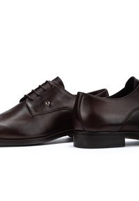 Zapatos de vestir de cuero marrón con textura suave, punteras redondeadas, diseño de cordones y un pequeño logo decorativo en el lateral. Suelas de goma.