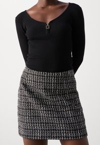 Top nero a righe con maniche lunghe, scollo a V e dettaglio con zip, abbinato a una gonna mini tessuta nero e bianco con texture.