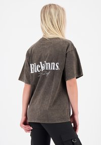 Bruine oversized t-shirt van katoen, met een vervaagde textuur en het "Blckwns" logo in het wit op de achterkant. Korte mouwen en een ronde hals.