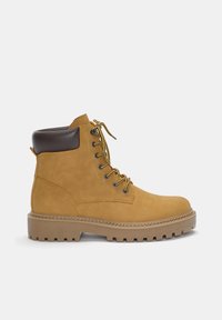 Stivaletto in suede beige con colletto in pelle marrone, occhielli in metallo, lacci gialli e suola spessa in gomma con battistrada pronunciato.