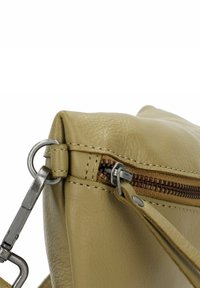 Angolo di una borsa in pelle beige con chiusura metallica e zip marrone, che mostra una cucitura dettagliata e un tirante della zip.