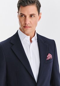 Granatowa marynarka o fakturowanej tkaninie, biała koszula z kołnierzykiem oraz różowa poszetka z motywem kwiatowym, tworzące elegancki wygląd.