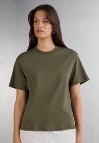 Olivově zelené tričko s krátkým rukávem, kulatým výstřihem a volným střihem, vyrobené z hladké, lehké tkaniny. Jednoduchý design, minimální švy.