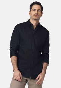 Czarna koszula zapinana na guziki, wykonana z materiału o teksturowanej powierzchni, z klasycznym kołnierzykiem, długimi rękawami i małą kieszonką na piersi.