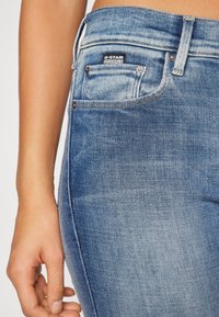 Jeans de mezclilla azul con cintura alta, que presentan un pequeño bolsillo frontal, costuras en contraste y una etiqueta con la inscripción "G-STAR ORIGINALS".