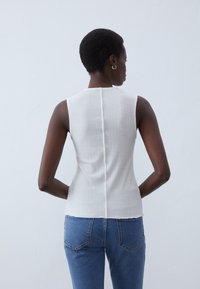 Valge ribaga ilma varrukateta topp kõrge kaelusega, millel on keskmine seljaõmblus. Koos siniste denim teksadega.