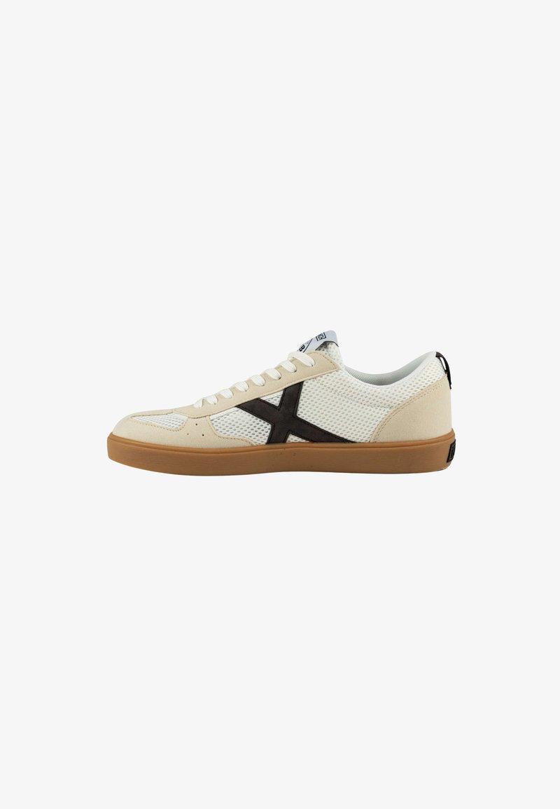 Zapatilla deportiva blanca y beige con parte superior de malla transpirable, detalle del logo en marrón oscuro y suela de goma. Presenta un cierre con cordones.