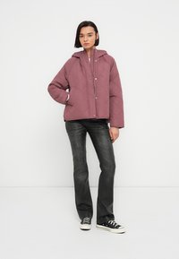 Παλτό με επένδυση καπιτονέ και κουκούλα σε σκόπιμο ροζ χρώμα, με κουμπιά πατιλέτας και κουβερτοειδές σχήμα. Φορεμένο με σκούρα τζιν και μαύρα αθλητικά παπούτσια.