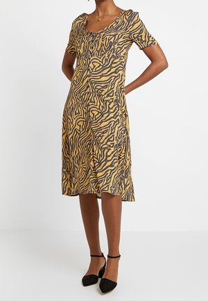 Lyhythihainen mekko keltaisena mustalla tiikeriraitakuviolla, jossa on V-aukko ja kevyet lievät poimutukset hartioilla, valmistettu kevyestä kankaasta.