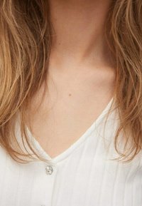 Long light brown hair framing a neck and upper chest wearing a white V-neck buttoned shirt.