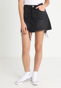 Black denim mini skirt with frayed hem, high-waisted design, five-pocket style, paired with white high-top sneakers.