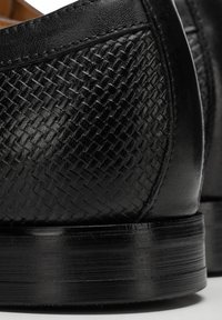 Schwarze Lederschuhe mit gewebter Textur und glatten Akzenten, mit abgerundetem Zehenbereich und stabilem Holzabsatz. Detailreiche Naht sichtbar.