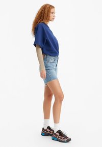 Sudadera de gran tamaño en color navy, pantalones cortos de denim azul claro con dobladillo deshilachado, zapatillas deportivas negras y azules, calcetines blancos hasta el tobillo, camiseta de manga larga texturizada debajo.