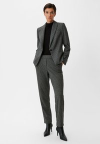 Gray checkered suit featuring a tailored blazer and slim trousers, complemented by a black turtleneck. Black heeled ankle boots complete the look.