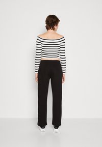 Pantalon large noir associé à un top court à rayures noir et blanc, sans épaule. Tissu lisse avec une texture côtelée.