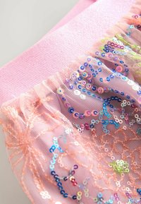 Un tissu en maille rose pailleté présente des sequins ronds colorés, avec un bord texturé et froncé et une taille élastique rose scintillante.