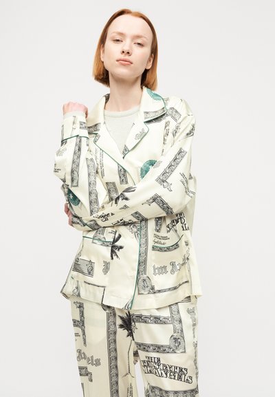 Νεαρός με κοντά κόκκινα μαλλιά, φορώντας μπεζ σύνολο με τύπωμα σχεδίων χαρτονομισμάτων δολαρίου και φοίνικες.