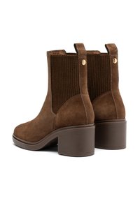 Botas de tobillo de ante marrón con paneles laterales elásticos y un tacón de bloque. Presentan un diseño acanalado texturizado y acentos en tono dorado.