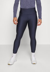 Marineblå treningsleggings med høy liv, laget av elastisk materiale. Kombinert med hvite joggesko og ankel-lange sokker.