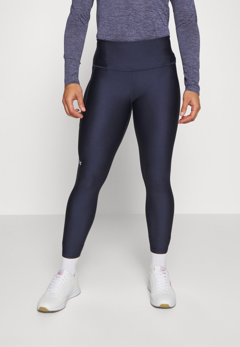 Marineblå treningsleggings med høy liv, laget av elastisk materiale. Kombinert med hvite joggesko og ankel-lange sokker.