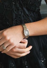 Silberne und goldfarbene Metall-Uhr mit rechteckigem Ziffernblatt, schwarzem Ziffernblatt mit römischen Ziffern und strukturiertem Armband.