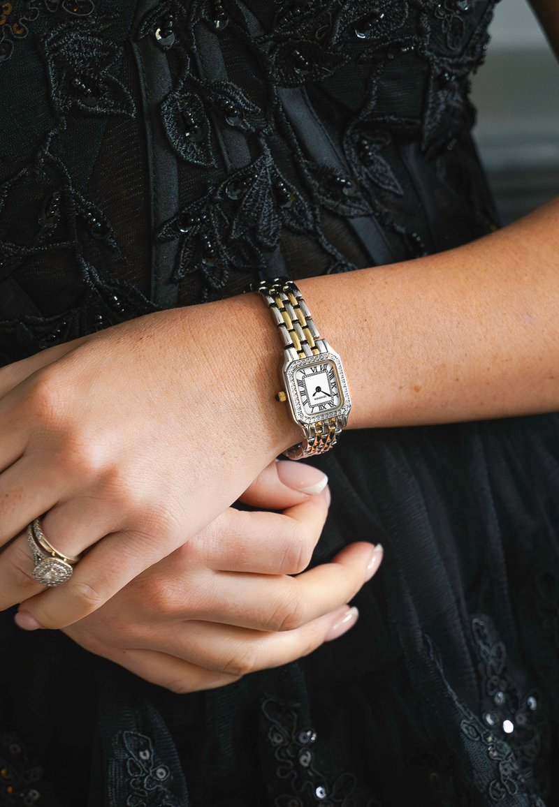 Silberne und goldfarbene Metall-Uhr mit rechteckigem Ziffernblatt, schwarzem Ziffernblatt mit römischen Ziffern und strukturiertem Armband.