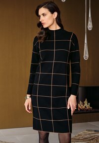 Svart klänning med orange rutmönster, hög krage, långa ärmar och figursydd passform, tillsammans med ett silverarmband och svarta strumpbyxor.