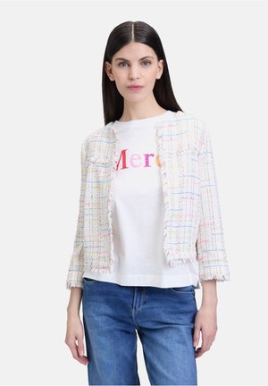 Tweed-Jacke in Pastellfarben mit fransigem Saum, kombiniert mit einem weißen T-Shirt mit pinkem Text. Das Model trägt blaue Jeans.